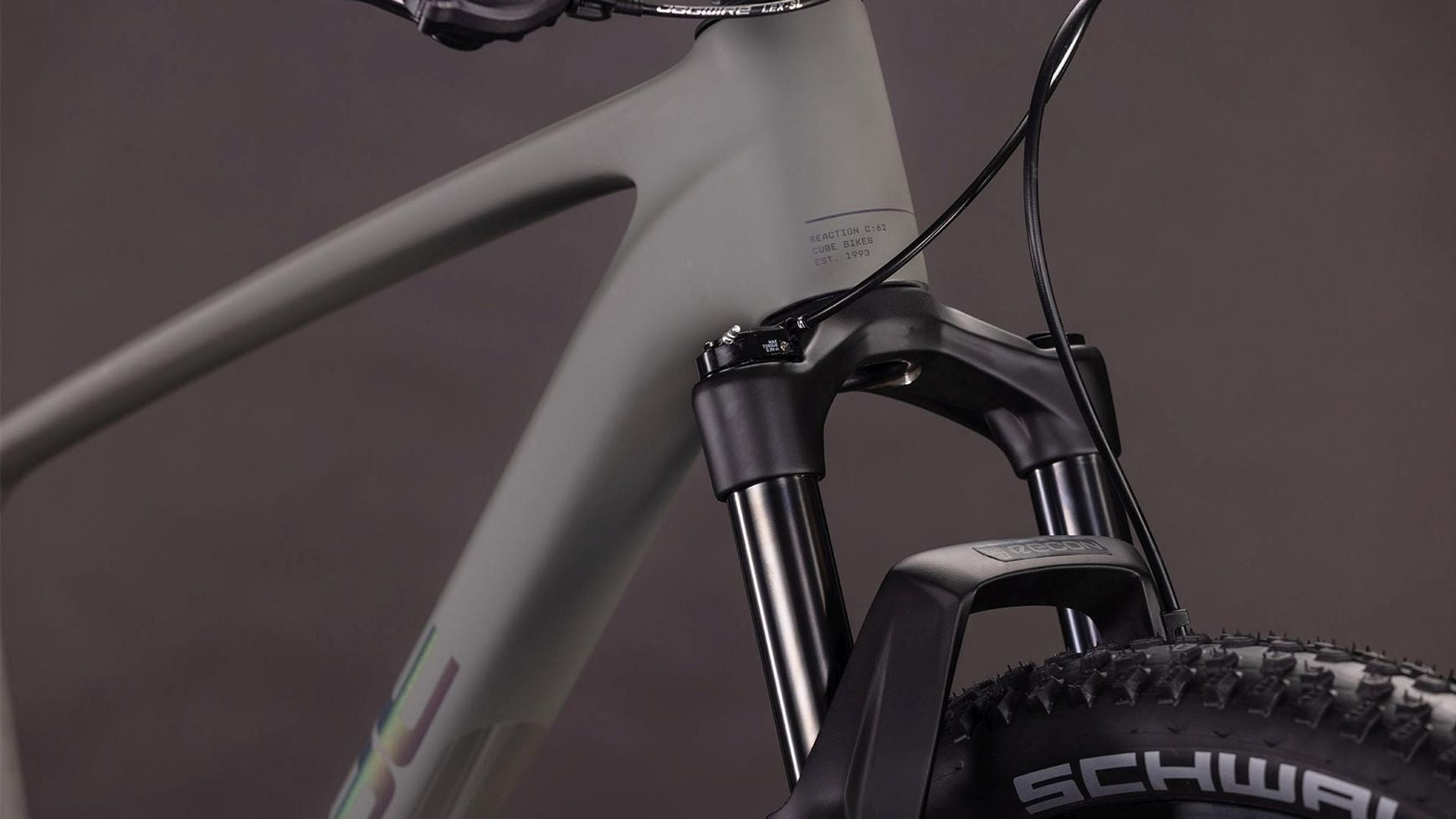 Nahaufnahme des vorderen Rahmens und der Federgabel des CUBE Reaction C:62 ONE. Zu sehen sind der C:62 Carbon-Rahmen, die RockShox Recon Silver Luftfedergabel, ein Teil des Lenkers mit Zügen und ein Schwalbe-Reifen vor einem dunklen Hintergrund.